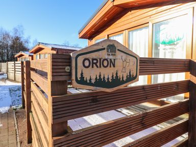 A wooden cabin with a wooden fence and a sign saying Orion at Felmoor Park