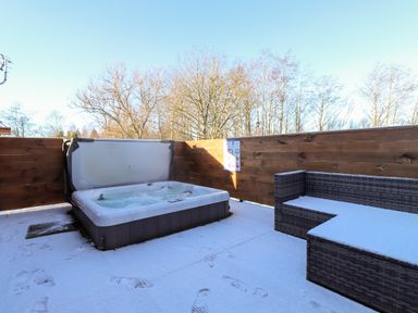 An outdoor patio with a hot tub and wicker sofa covered in snow at Orion in Felmoor Park
