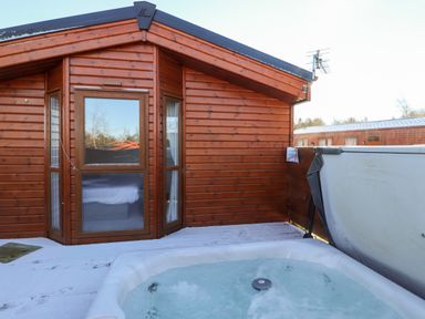 A wooden cabin exterior with windows and a hot tub on a snowy deck at Orion in Felmoor Park