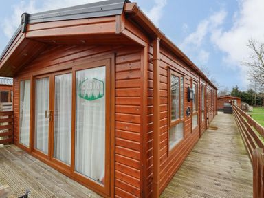 An exterior view of a wooden cabin with large glass doors and windows on a wooden deck at Orion in Felmoor Park