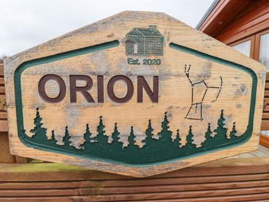 A carved wooden sign with the word Orion trees an outline of a cabin and a constellation at Orion in Felmoor Park
