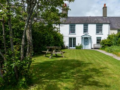 A garden with a wooden picnic table and a path leading to a white house at Tros Yr Afon in Beaumaris