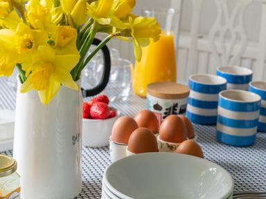 A table set with yellow flowers in a white vase eggs in egg cups strawberries orange juice and blue striped mugs at Tros Yr Afon in Beaumaris