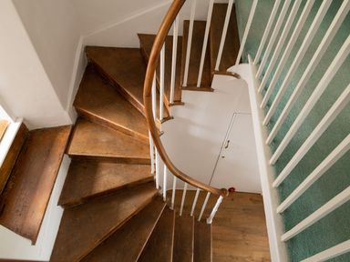 A spiral wooden staircase with white balusters and green carpet on the adjacent floor at Tros Yr Afon in Beaumaris