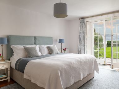 A bedroom with a double bed bedside tables with lamps and glass doors opening to a garden at Tros Yr Afon in Beaumaris