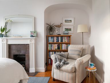 A reading corner with an armchair next to a bookshelf and a floor lamp in a bedroom at Tros Yr Afon in Beaumaris