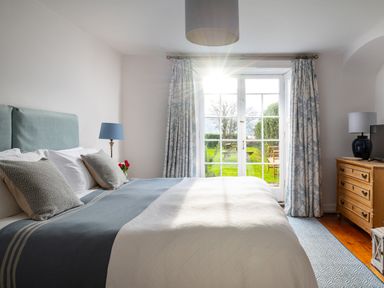 A bedroom with a bed and pillows next to glass doors opening to a garden at Tros Yr Afon in Beaumaris