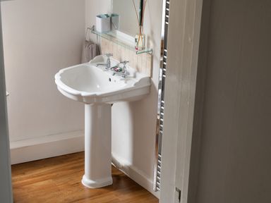 A bathroom with a pedestal sink towel holder mirror and a wooden floor at Tros Yr Afon in Beaumaris