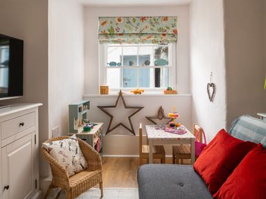 A small play area with a toy kitchen table and chairs under a window with floral curtains at Tros Yr Afon in Beaumaris