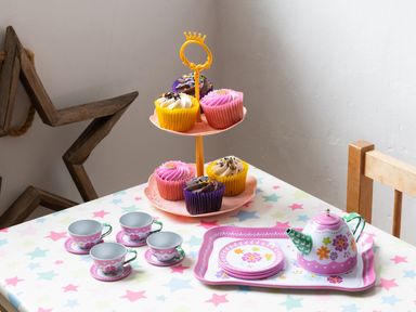 A table with a toy tea set and cupcakes on a two-tiered stand in a room with wooden furniture at Tros Yr Afon in Beaumaris