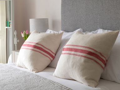 A bed with two pillows with red stripes a bedside table with a lamp and flowers at Tros Yr Afon in Beaumaris