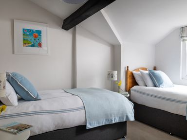 A bedroom with two single beds blue pillows and a bedside table with a lamp and flowers at Tros Yr Afon in Beaumaris