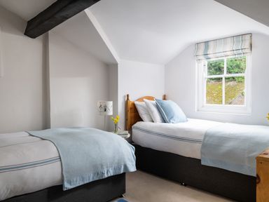A bedroom with two single beds and a window with striped blinds at Tros Yr Afon in Beaumaris