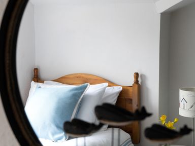 A wooden bed with white and blue pillows reflected in a round mirror with whale decorations at Tros Yr Afon in Beaumaris