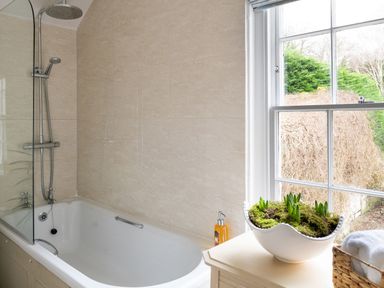 A bathroom with a bathtub shower combination next to a window with a plant on a cabinet at Tros Yr Afon Beaumaris