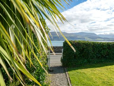 A garden path between green hedges leading to a gate with a view of water and mountains at Tros Yr Afon in Beaumaris