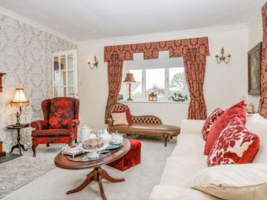 A living room with red patterned curtains a leather chaise lounge a red and black armchair a cream sofa with red patterned cushions and a wooden coffee table with tea set at Storrs Lodge in Bowness-On-Windermere