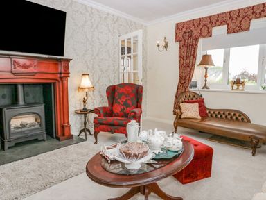 A living room with a fireplace armchair chaise lounge coffee table and window at Storrs Lodge in Bowness-On-Windermere