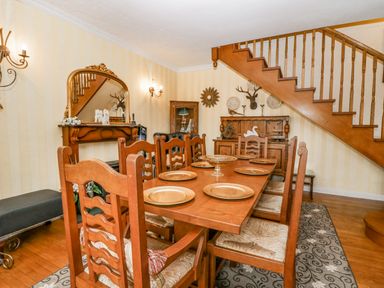 A dining room with wooden table and chairs beneath a wooden staircase with decorative plates and a mounted deer head at Storrs Lodge Bowness-On-Windermere