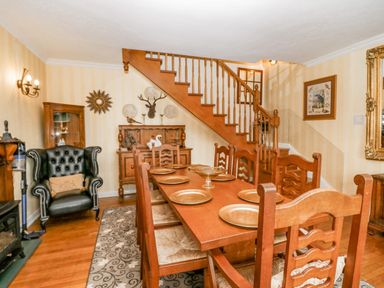 A dining room with wooden table and chairs under a staircase with decorative plates on the wall at Storrs Lodge in Bowness-On-Windermere