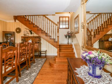 A dining room with wooden chairs a wooden staircase and a floral arrangement in a blue and white vase at Storrs Lodge in Bowness-On-Windermere