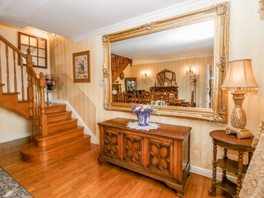 A wooden staircase beside a sideboard with a flower vase under a large decorative mirror and a lamp on a small round table at Storrs Lodge in Bowness-On-Windermere
