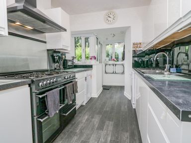 A galley kitchen with black countertops white cabinets a black gas range and a stainless steel sink at Storrs Lodge in Bowness-On-Windermere