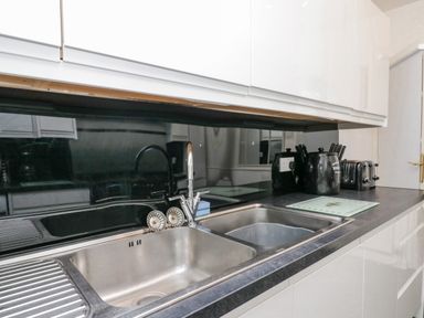 A kitchen countertop with a double stainless steel sink a black backsplash and black kitchen appliances at Storrs Lodge in Bowness-On-Windermere