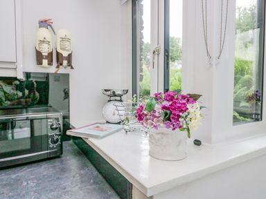 A kitchen corner with a microwave a scale a cookbook and a flower pot on a countertop at Storrs Lodge in Bowness-On-Windermere