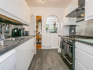 A galley kitchen with black appliances and white cabinets at Storrs Lodge in Bowness-On-Windermere