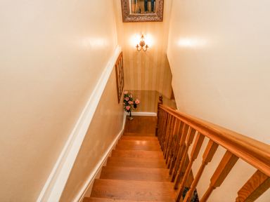Wooden staircase with railing leading to a floor with a bouquet of flowers near a wall with a light fixture and framed picture at Storrs Lodge in Bowness-On-Windermere