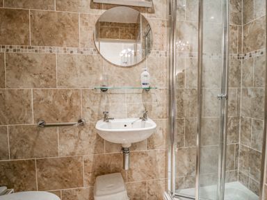 A bathroom with a wall-mounted sink mirror glass shelf and shower enclosure at Storrs Lodge in Bowness-On-Windermere