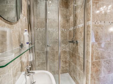 A bathroom with a glass shower enclosure a sink with a faucet and a shelf with toiletries at Storrs Lodge in Bowness-On-Windermere