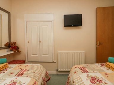 A bedroom with two beds a wall-mounted television a closed closet door a radiator a wooden door and a teddy bear on a shelf at Storrs Lodge in Bowness-On-Windermere
