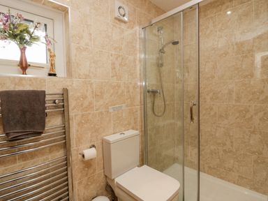 A bathroom with a toilet a glass shower enclosure a towel rack with a towel and a small window with flowers and a statue at Storrs Lodge in Bowness-On-Windermere