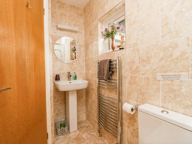 A bathroom with a pedestal sink round mirror towel rack with towel and a toilet at Storrs Lodge in Bowness-On-Windermere