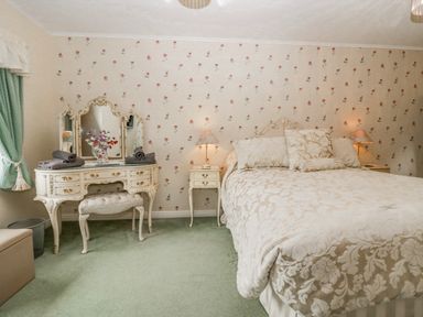 A bedroom with a double bed bedside tables a vanity table with mirror and stool and green curtains at Storrs Lodge Bowness-On-Windermere