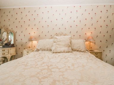 A bedroom with a large bed two bedside tables with lamps and a dresser with a mirror at Storrs Lodge in Bowness-On-Windermere