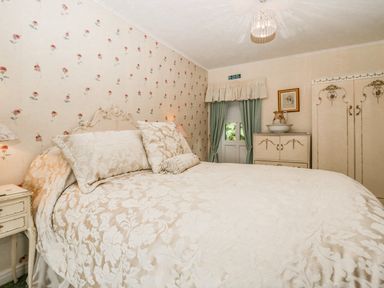 A bedroom with a bed with floral bedding a nightstand a cabinet and wallpaper at Storrs Lodge in Bowness-On-Windermere
