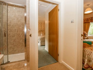 A hallway with an open wooden door showing a bedroom and a tiled shower room at Storrs Lodge in Bowness-On-Windermere