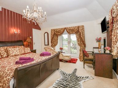 A bedroom with a patterned bedspread purple towels a chandelier a wooden desk a chair and French doors at Storrs Lodge in Bowness-On-Windermere
