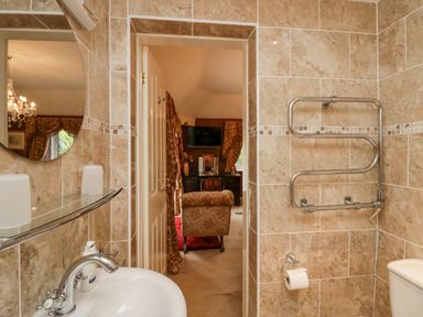 A bathroom with a sink a towel warmer and a toilet looking into a room with an armchair and a television at Storrs Lodge in Bowness-On-Windermere