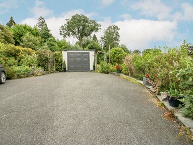 A driveway leading to a garage surrounded by plants and trees at Storrs Lodge in Bowness-On-Windermere