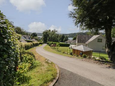 A winding road with houses and greenery with a lake and hills in the background at Storrs Lodge in Bowness-On-Windermere