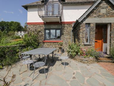 A stone patio with a metal table and chairs outside a stone and white house at Storrs Lodge in Bowness-On-Windermere