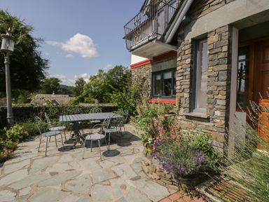 An outdoor patio area with metal table and chairs stone walls and garden plants at Storrs Lodge in Bowness-On-Windermere