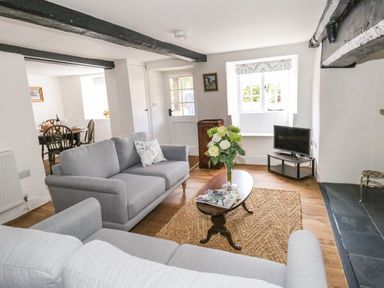 A living room with grey sofas wooden coffee table flowers on table and a small tv at Lime Cottage in Burton Bradstock