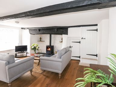 A living room with two grey sofas a wood-burning stove and wooden beams at Lime Cottage in Burton Bradstock