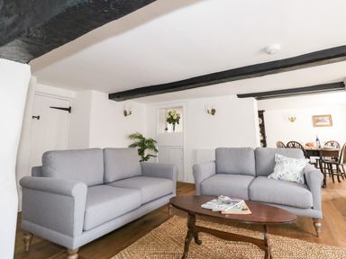 A living room with two gray sofas a wooden coffee table with magazines and a dining area visible in the background at Lime Cottage Burton Bradstock