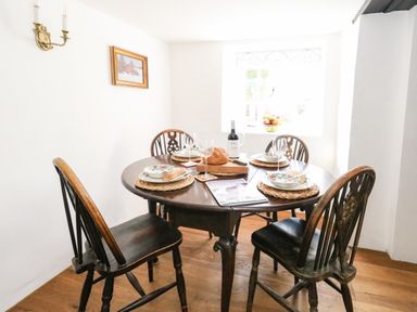 A dining area with a round wooden table set for four with plates bowls wine glasses and a bottle of wine at Lime Cottage Burton Bradstock